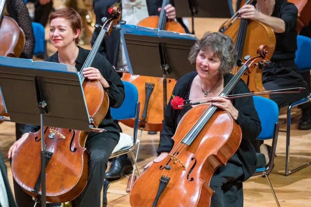 Elegant female cellist smiling during Sampson Orchestra performance in a concert hall.