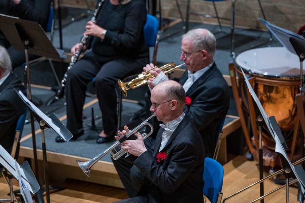 Elegant musicians of Sampson Orchestra performing with brass and wind instruments in a concert hall.