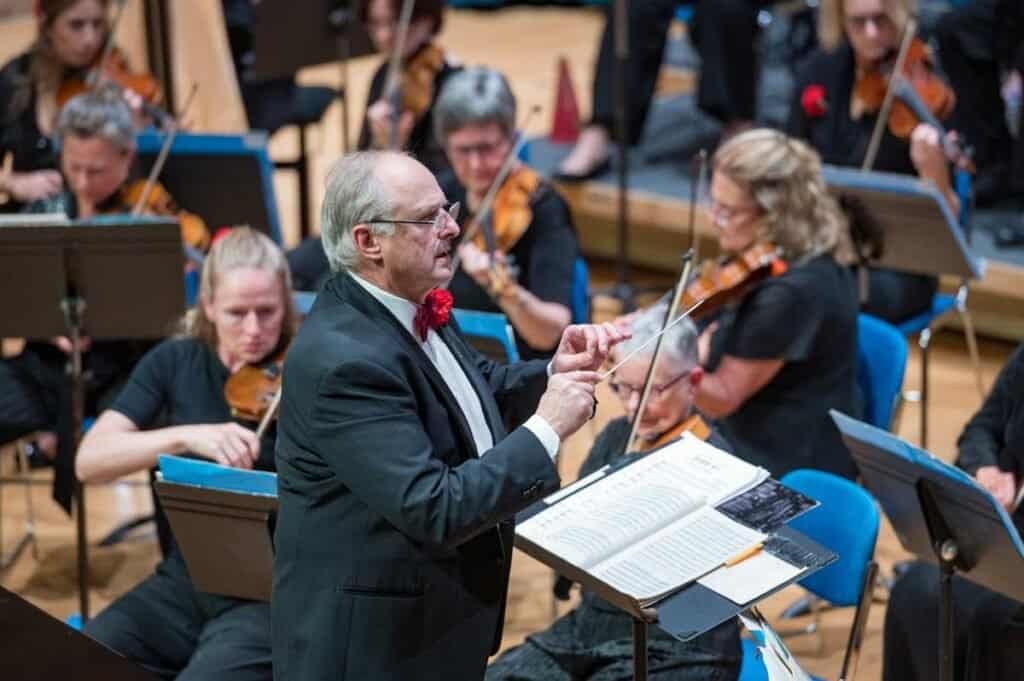 Orchestra conductor leading Sampson Orchestra performance in a concert hall.